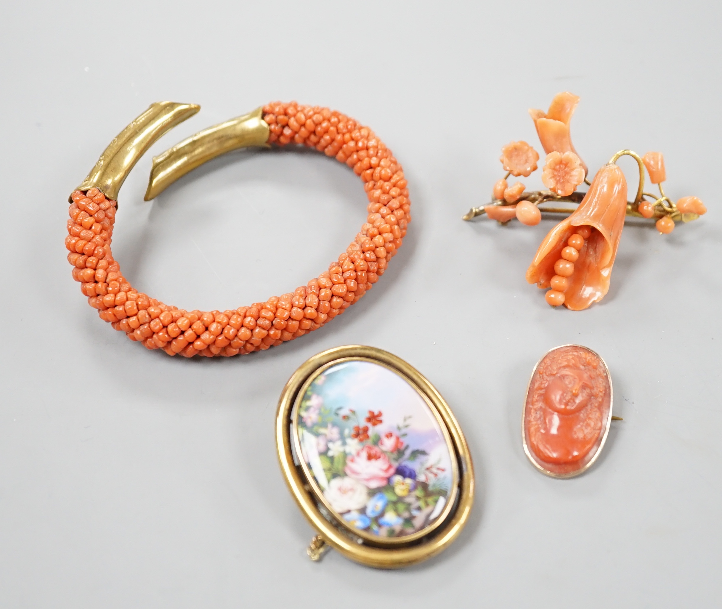 A yellow metal mounted carved coral oval brooch, 30mm, a mounted coral open bangle, a coral brooch and a gilt metal and enamelled brooch.